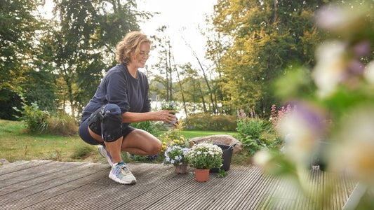 Woman kneeling while gardening. She is wearing Bauerfeind's GenuTrain OA Knee Brace